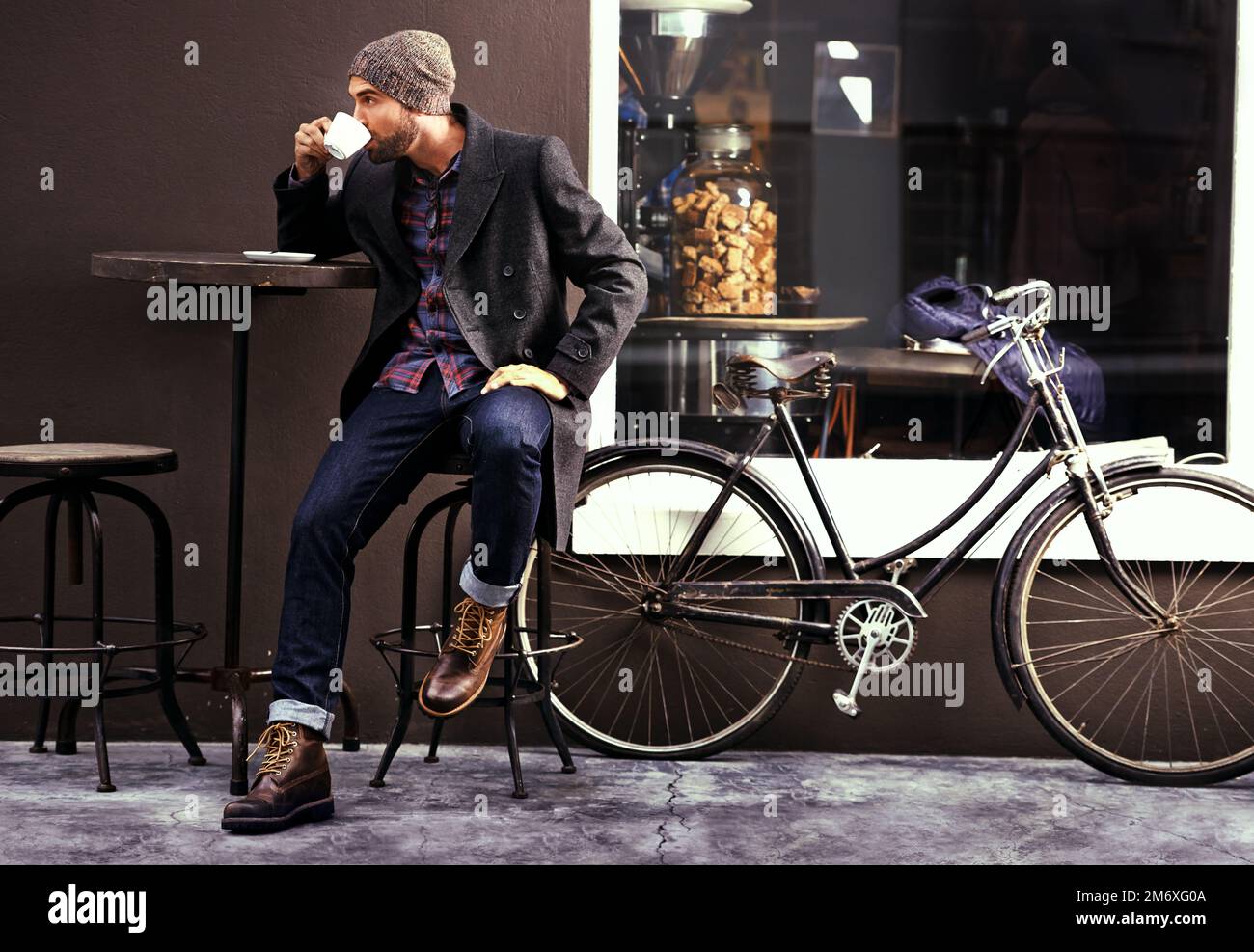 Caffè per rendere la giornata più lunga. un bel giovane che si gode una tazza di caffè in un bar della città mentre la sua bicicletta si trova accanto a lui. Foto Stock