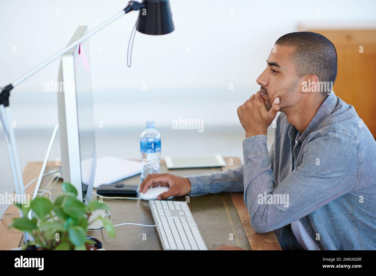 Ciò prenderà un certo serio pensiero. un bel giovane che lavora al suo computer in un ufficio. Foto Stock
