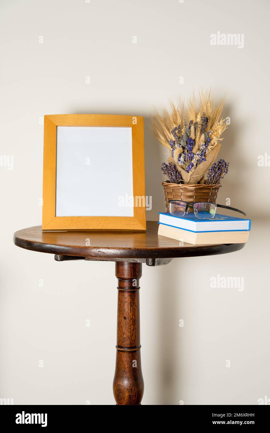 mockup stile di vita tavolo interno piedistallo con cornice vuota cestino di fiori secchi libri e occhiali Foto Stock