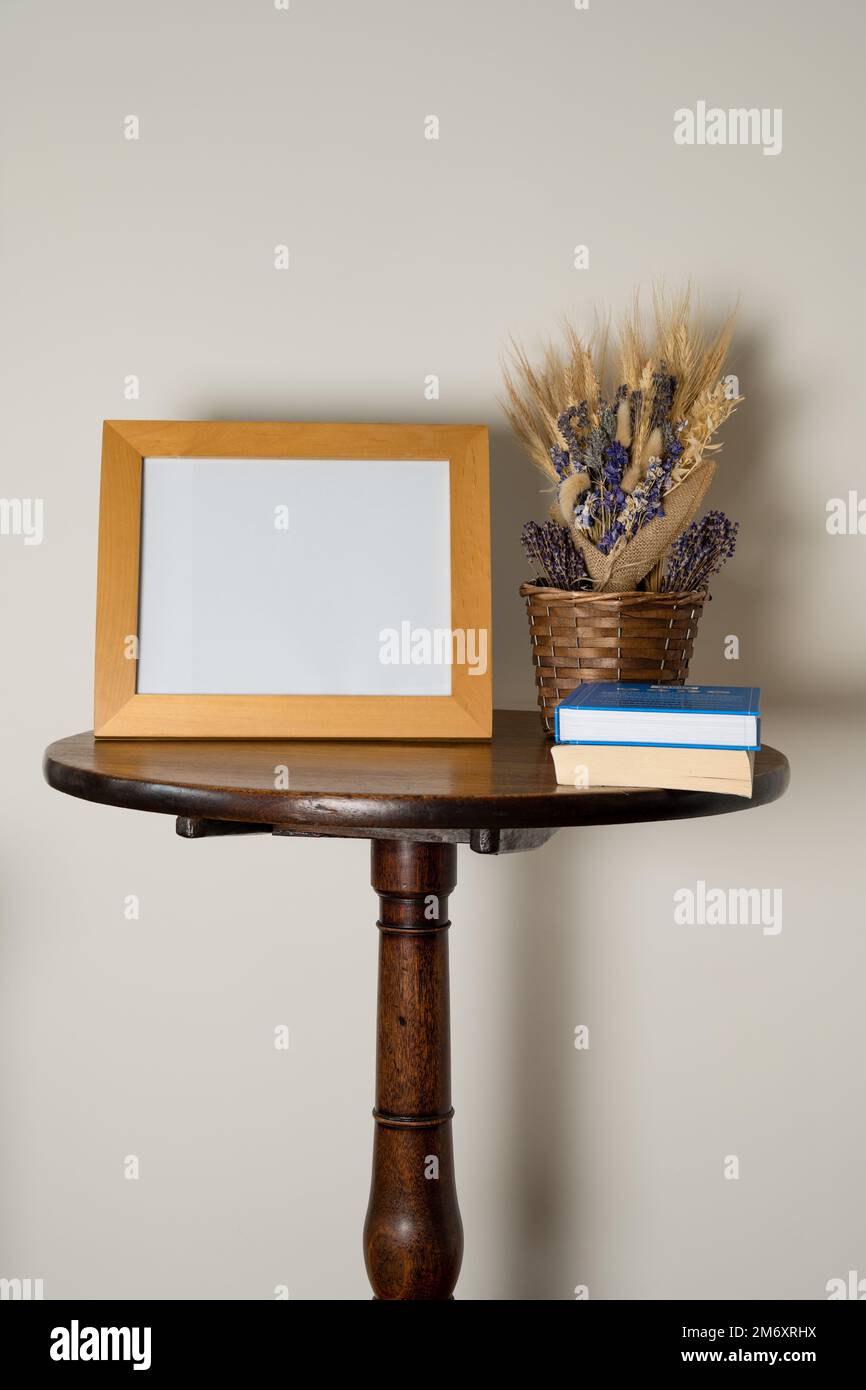 mockup stile di vita tavolo interno piedistallo con cornice vuota cesto di fiori secchi e libri Foto Stock