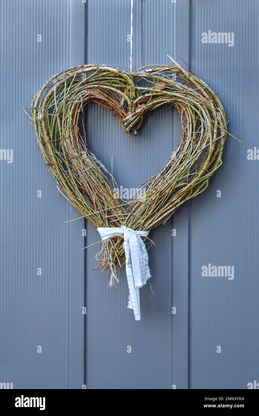 Rametti asciutti legati a forma di cuore appesi su una porta di legno grigio blu, simbolo di benvenuto per la gentilezza e l'amore, decorazione fatta in casa per San Valentino, copia Foto Stock
