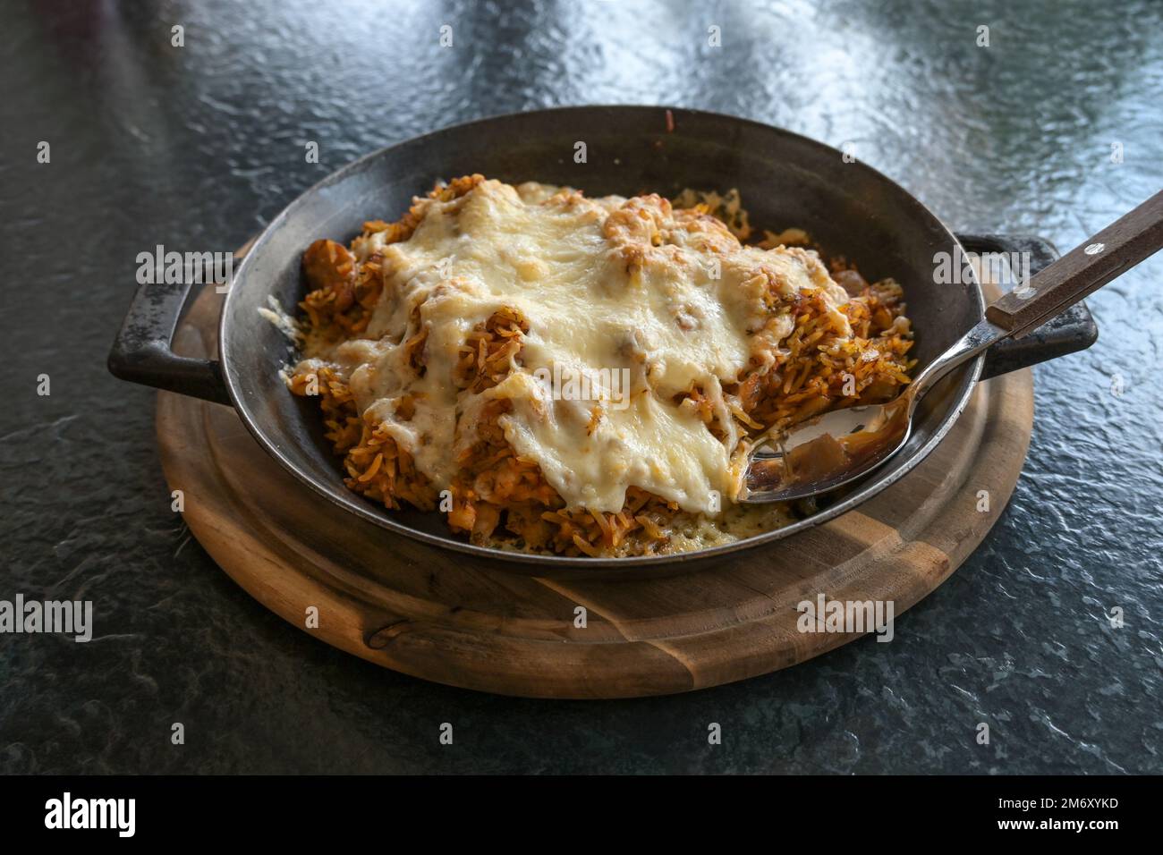 Riso fritto con spezie e condito con formaggio in una padella di ferro su un tagliere di legno e un tavolo nero, cibo di fusione, fuoco selezionato, profondità stretta di Foto Stock