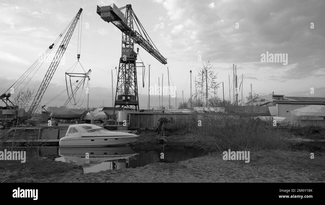 Gru dal cantiere navale nel porto industriale con riflesso di piccolo motoscafo bianco in acqua a Hard vicino a Bregenz in Austria in bianco e nero Foto Stock