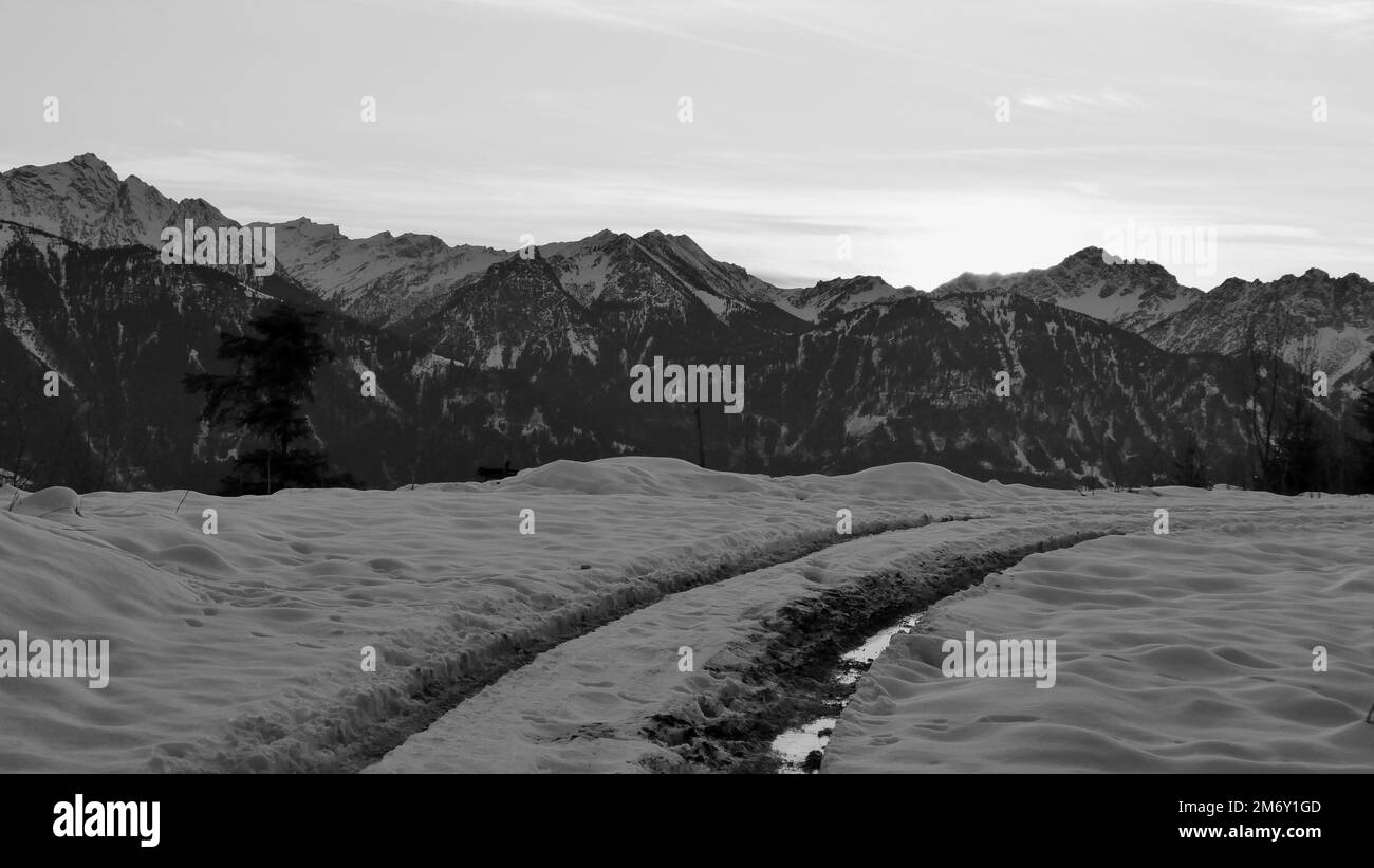 Gommisti su una strada di montagna con piccole pozze d'acqua nel fango e tramonto dietro le montagne in inverno in Austria in bianco e nero Foto Stock