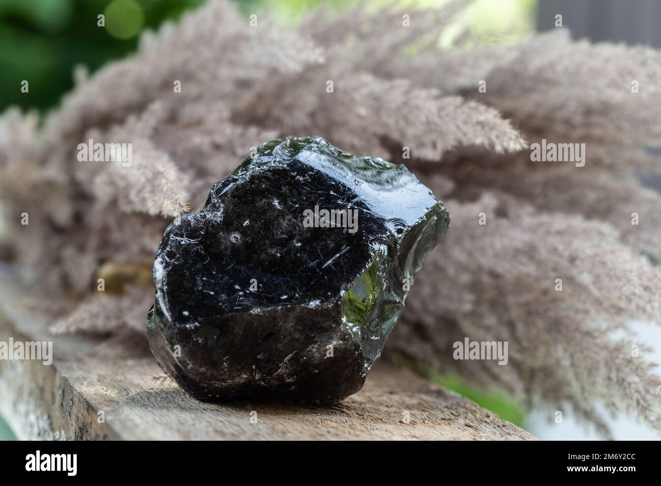 Campione di roccia minerale ossidiana nera su sfondo di legno. Forme vulcaniche naturali di vetro da Lava Foto Stock
