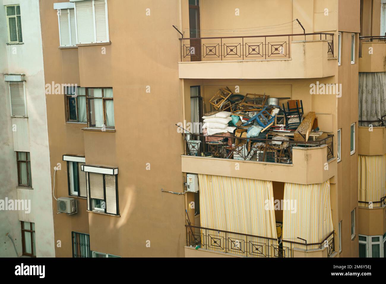Brutto, terribile disturbo del balcone. Edificio a più piani pieno di rifiuti, mobili vecchi, cose non necessarie, scatole, sedie, cuscini, vestiti, vetrata Foto Stock