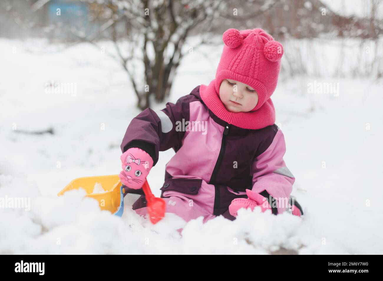 Adorabile ragazza scava neve con pala e secchio sul parco giochi coperto di neve. bambina che gioca in inverno all'aperto Foto Stock