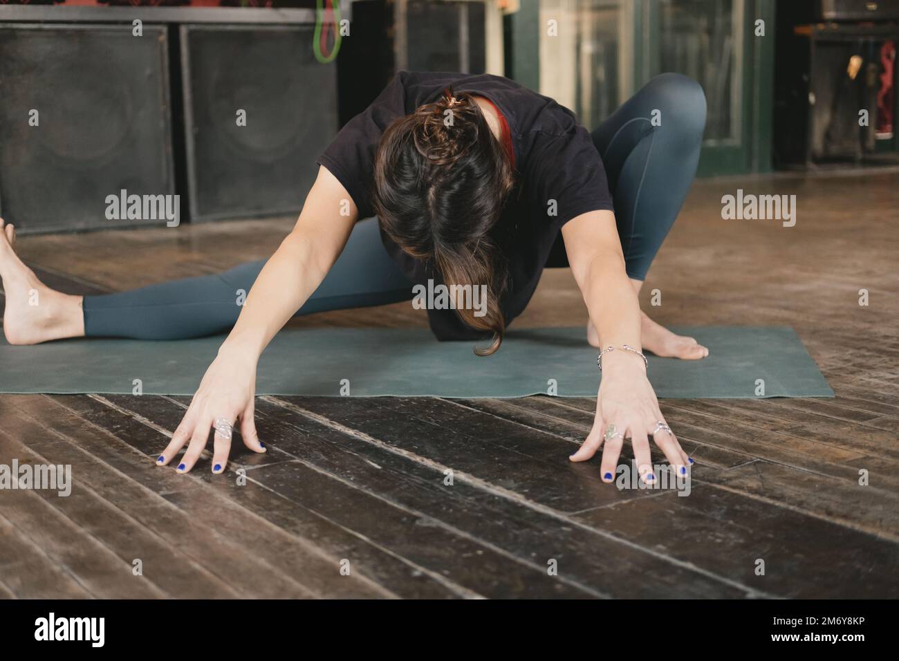 Donna irriconoscibile Yogi nuovo insegnante giovane adulto che fa una posa skandasana con piega in avanti e braccia estese con leggings verdi nella sua pratica di yoga Foto Stock