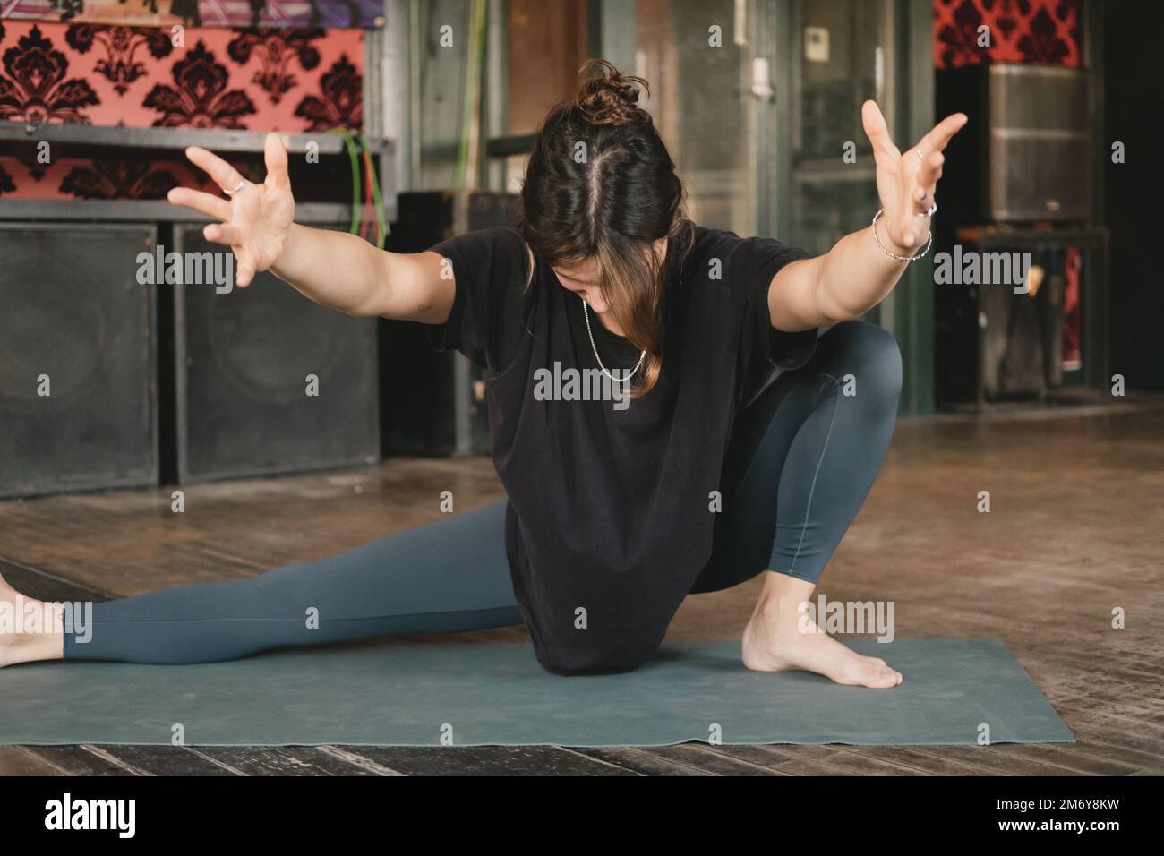 Donna Yogi nuova insegnante giovane adulto che bilancia una posa skandasana che si estende e tiene le braccia in aria con leggings verdi durante la sua pratica di yoga Foto Stock