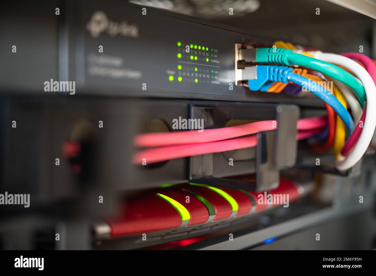 Router e switch con cavi LAN colorati in un cabinet di rete di un data center Foto Stock