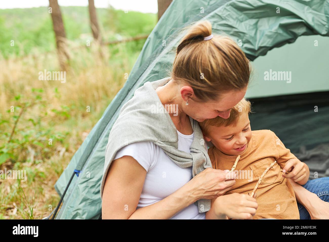 Madre e figlio giocano con bastoni mentre trascorrono del tempo libero in un campeggio nella foresta Foto Stock