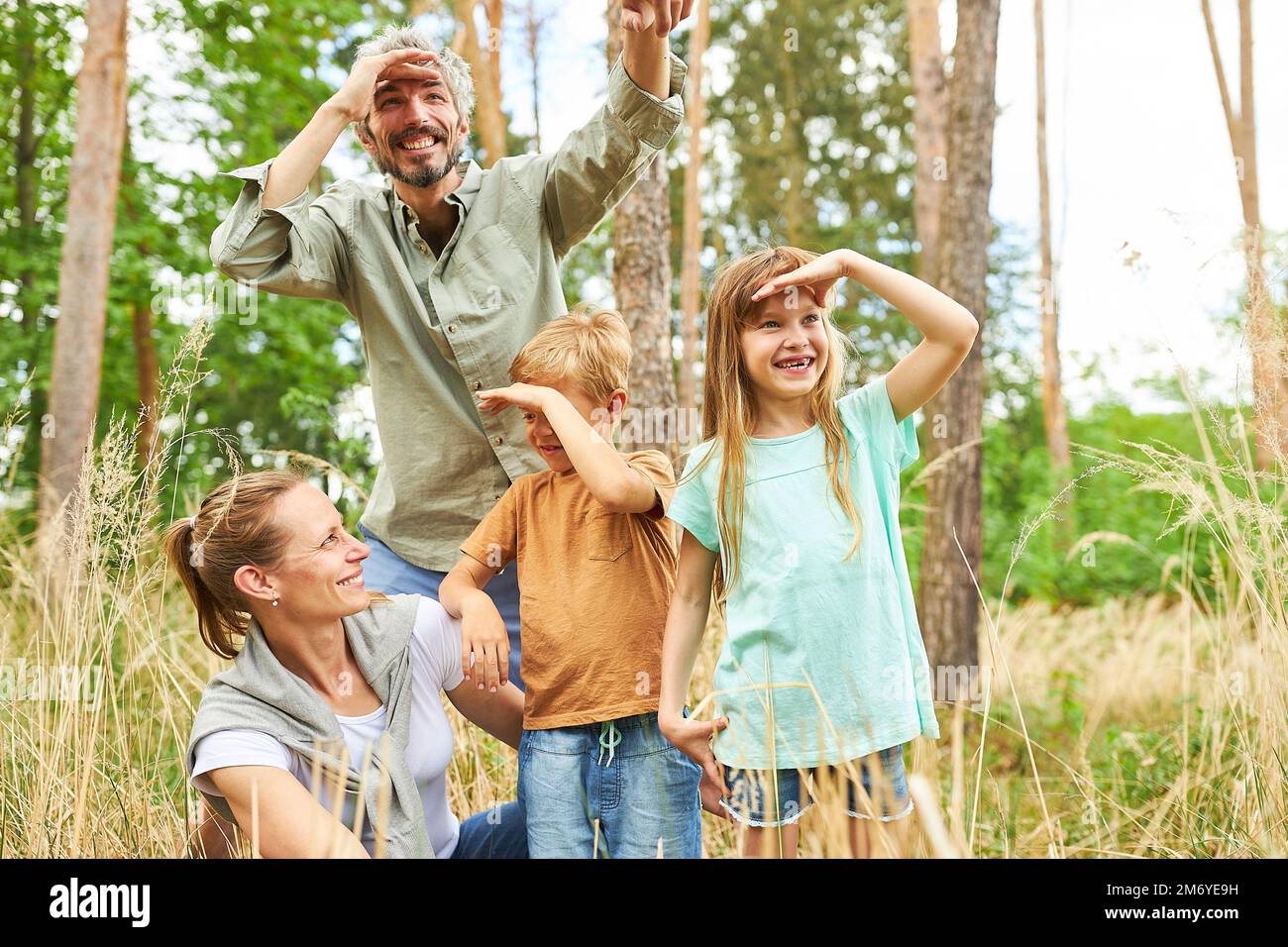 Genitori felici con figli e figlie che schermano gli occhi mentre esplorano la foresta durante le vacanze Foto Stock