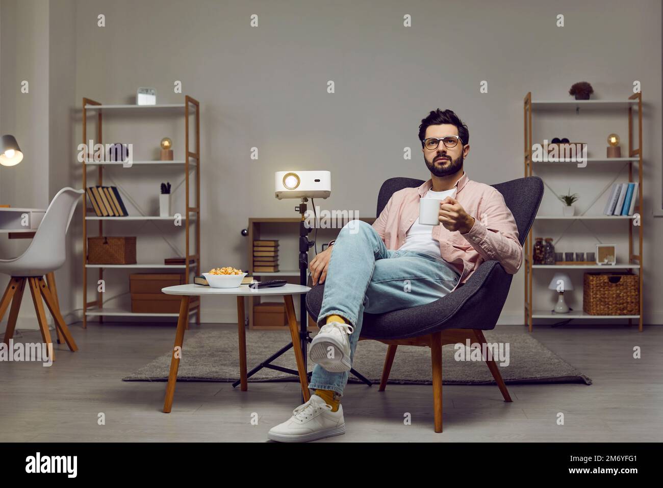Uomo seduto in poltrona a casa, con un proiettore, guardando un film e bevendo il tè Foto Stock