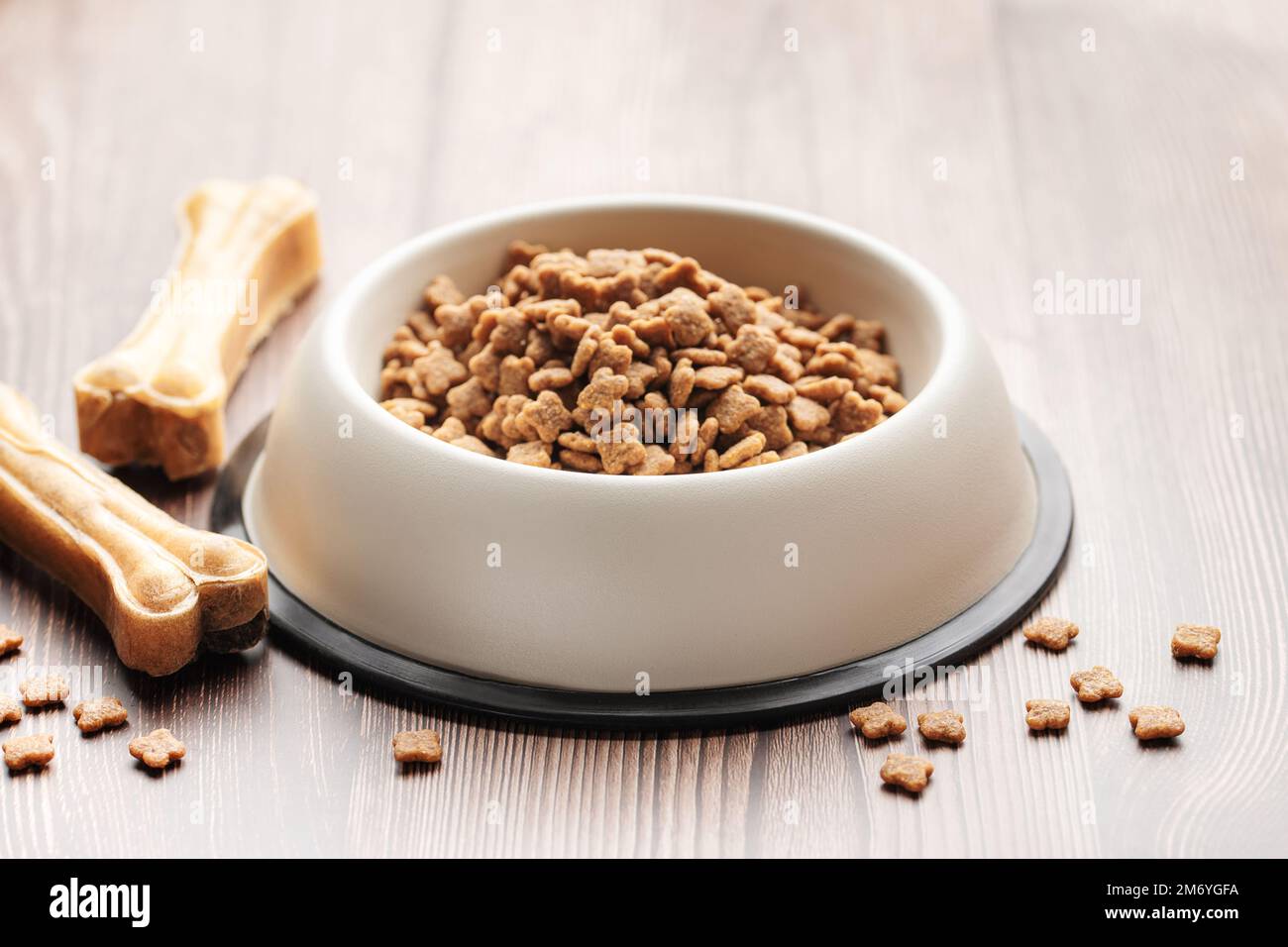 Una ciotola di cibo per cani e dolci sotto forma di ossa su un pavimento di legno. Cibo secco in granuli. Foto Stock