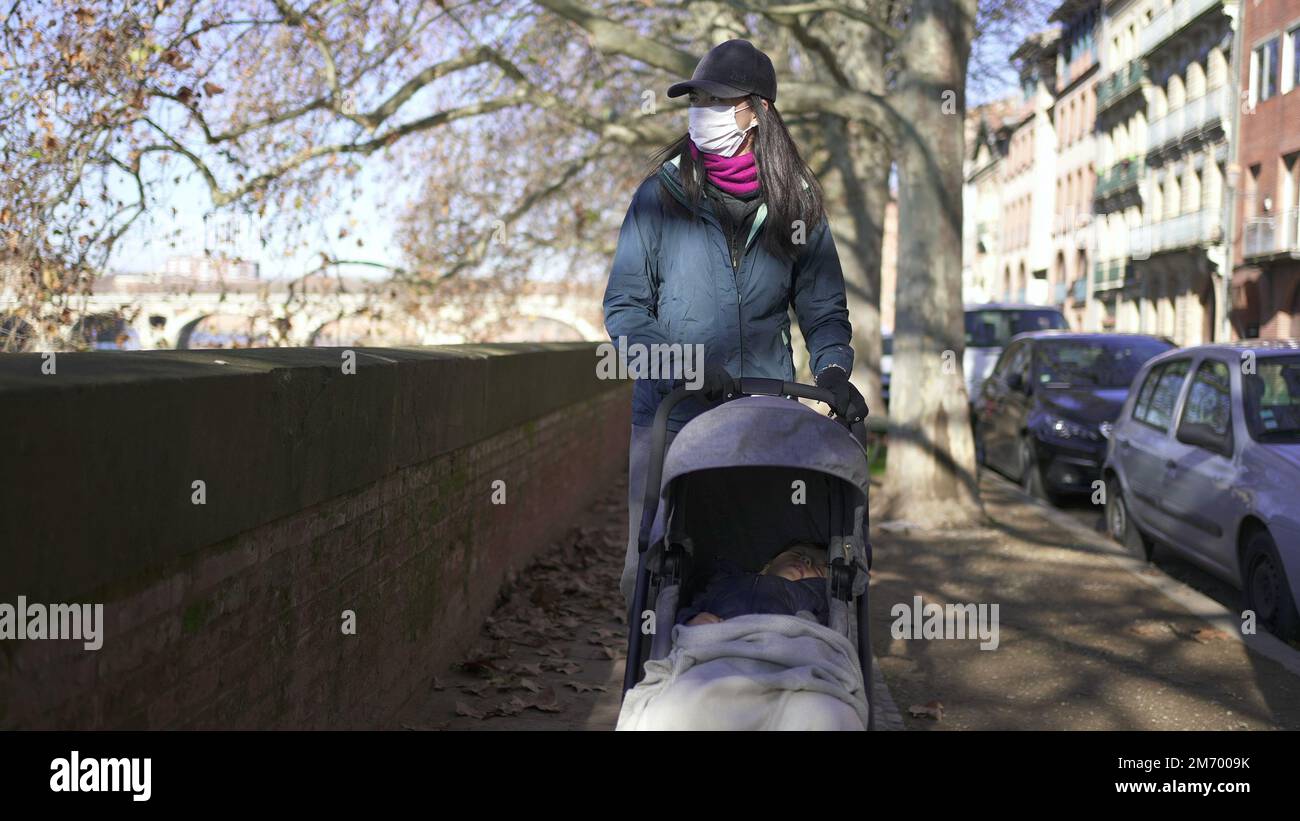 Tolosa, Francia, Gennaio 6 2020 - Madre che cammina all'aperto con passeggino mentre indossa una maschera facciale Foto Stock