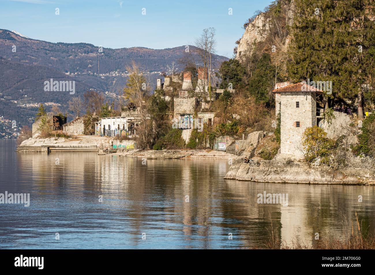 Castelveccana, Italia- 12-27-2022: Antichi forni in rovina con camini con mattoni rossi che si riflettono sull'acqua del Lago maggiore nel Parco delle Fornac Foto Stock