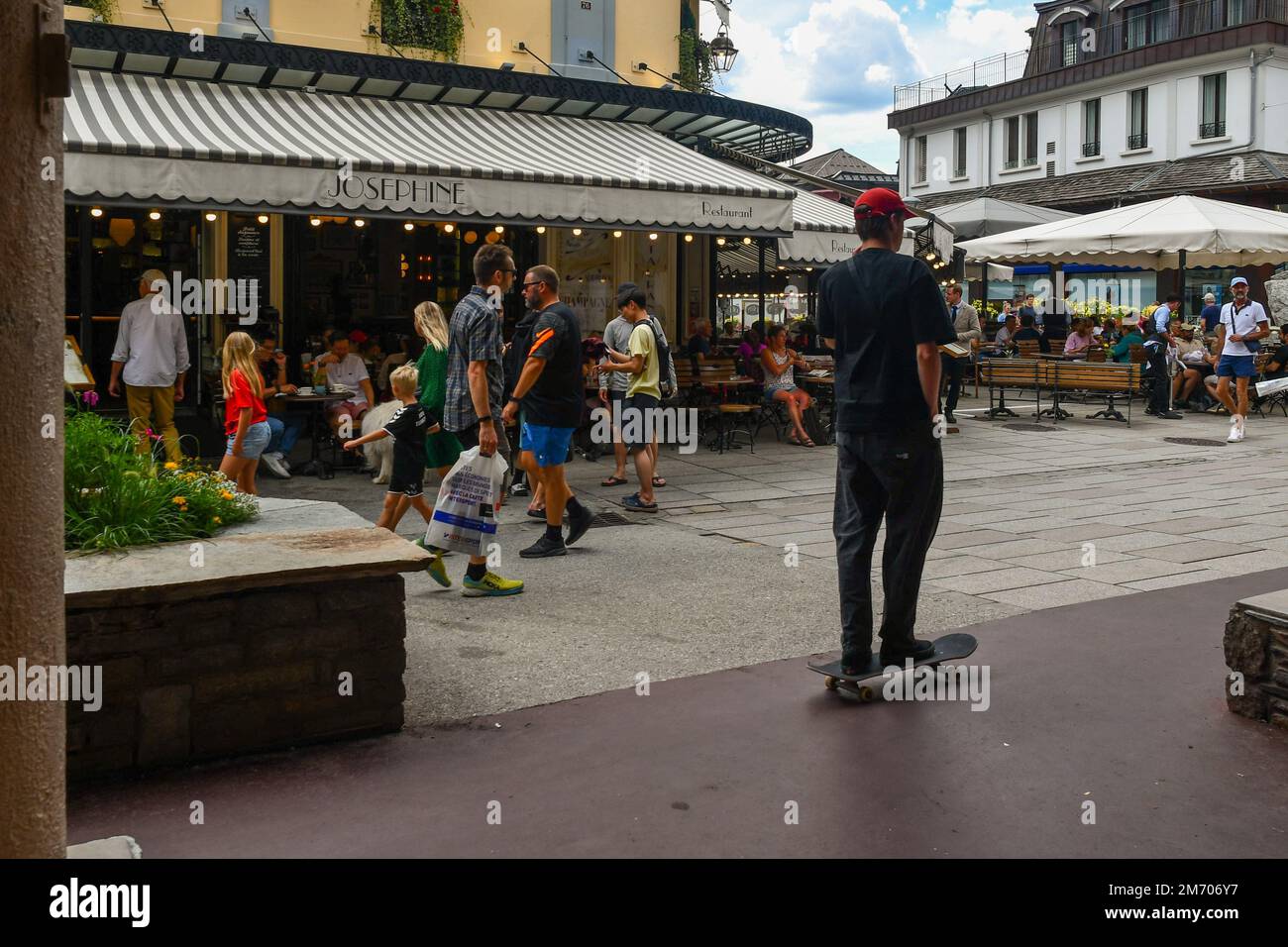 Vista sulla strada del centro della città alpina con i turisti a piedi e skatboarding di fronte a un tipico bistrot francese in estate, Chamonix, Francia Foto Stock