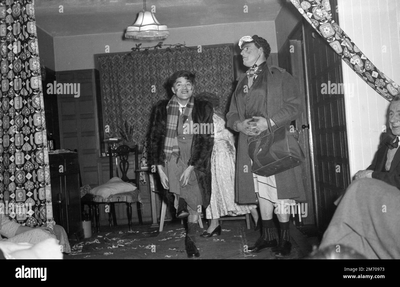 1950s, storico, divertimento festa a casa, in una stanza anteriore, due uomini in drag, vestito come donne, divertente membri della famiglia, Inghilterra, Regno Unito. Foto Stock