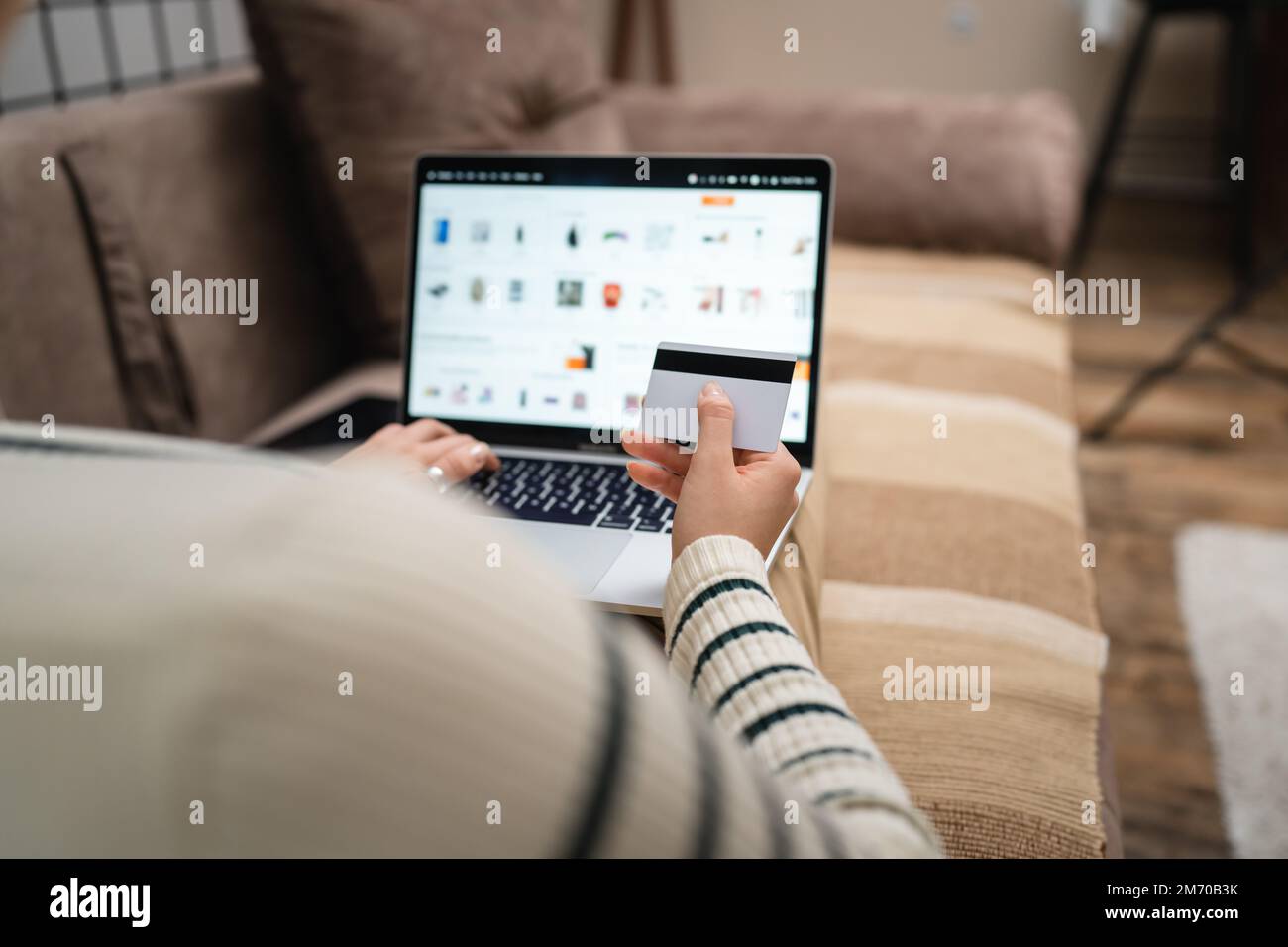 Una donna che acquista online tenere carta di credito e computer portatile a casa vista posteriore di giovane donna adulta fare l'acquisto online mentre si siede nel sof Foto Stock