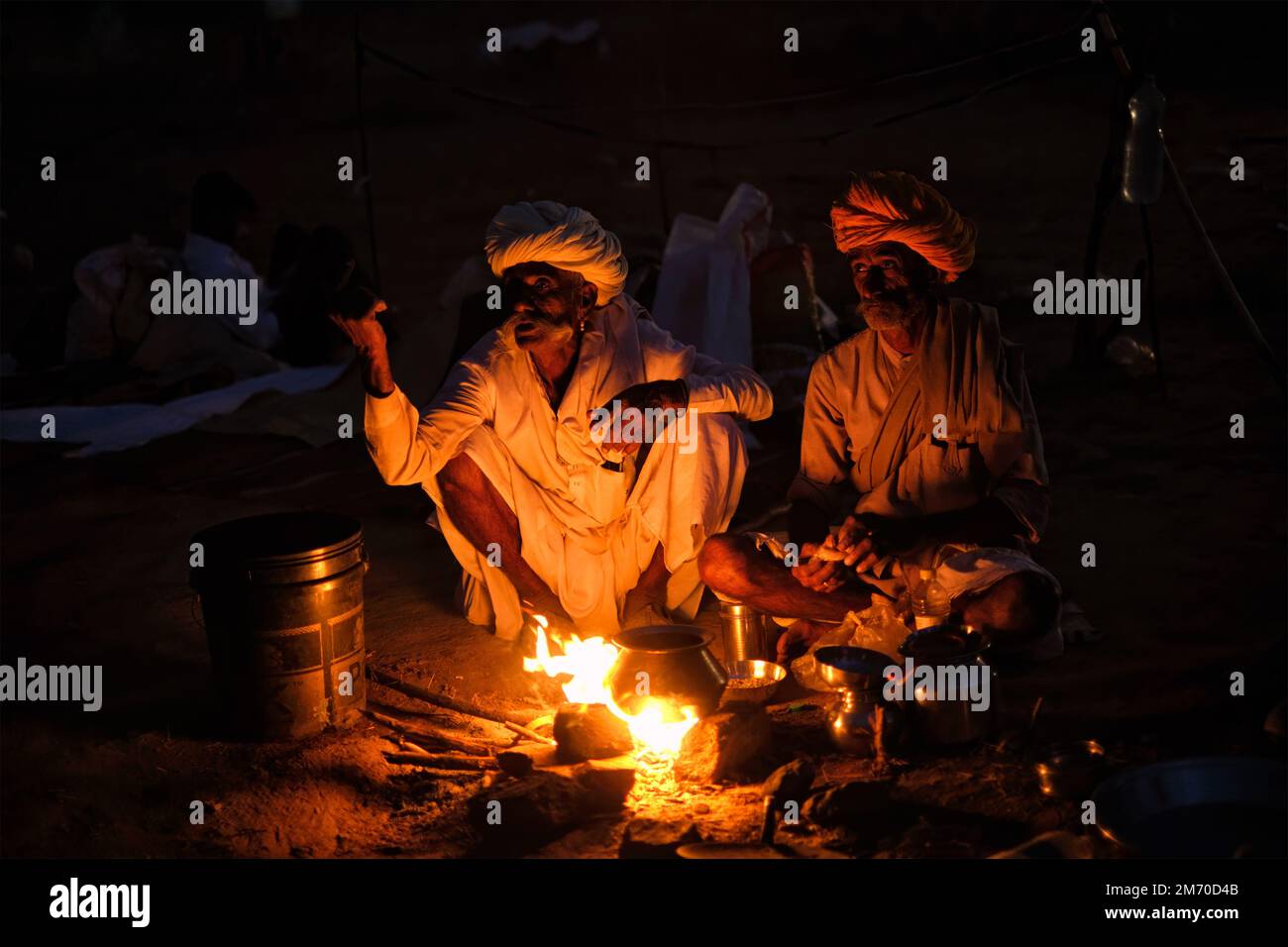 Pushkar, India - 6 novembre 2019: Uomini e cammelli del villaggio rurale indiano illuminati dal fuoco del campo di notte a Pushkar cammello fiera Pushkar Mela - annuale famoso ca Foto Stock