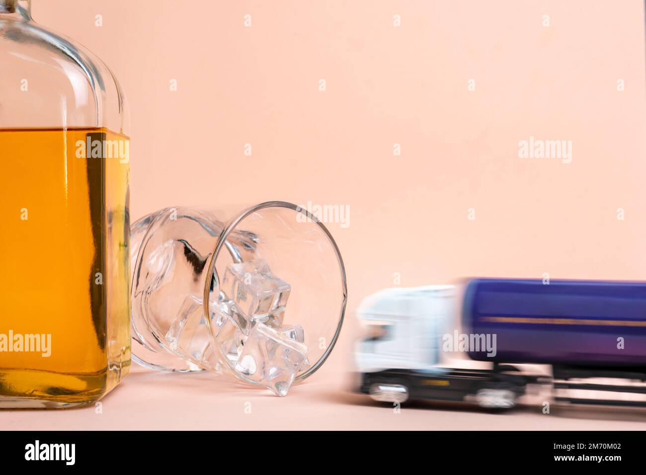 Una bottiglia di whiskey e un bicchiere sdraiati con cubetti di ghiaccio, un camion di autocisterna giocattolo ad alta velocità va verso il vetro per crash irrimediabilmente. Foto Stock