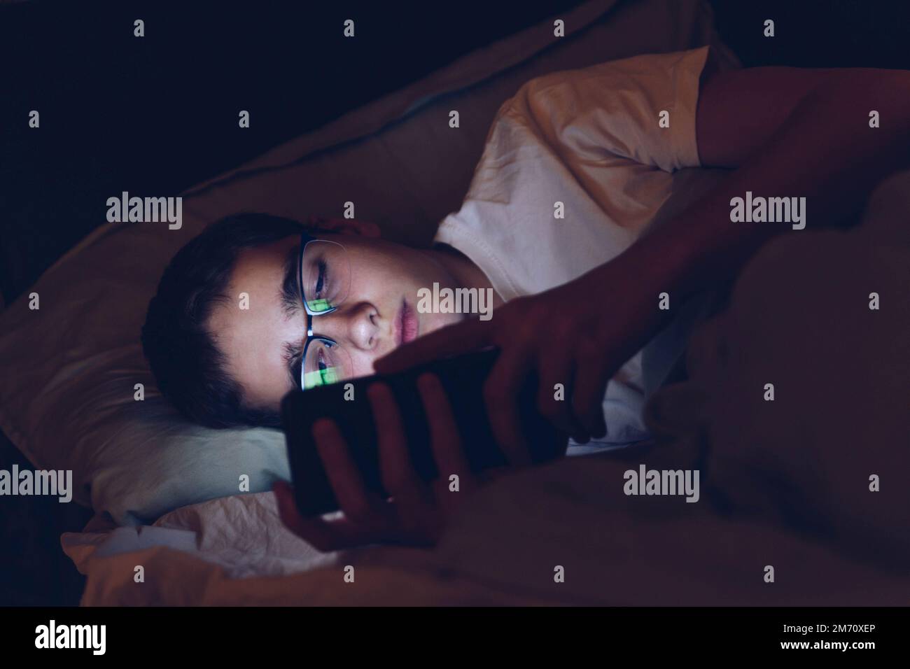 L'adolescente con gli occhiali usa il telefono a letto di notte. Foto Stock