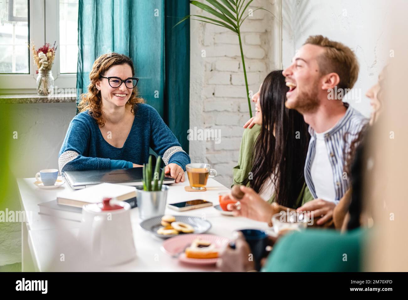 Donna felice sorridente mentre i suoi amici ridono, momenti spensierati di un giovane gruppo di studenti in una caffetteria, prima colazione e brunch in una letteraria Foto Stock