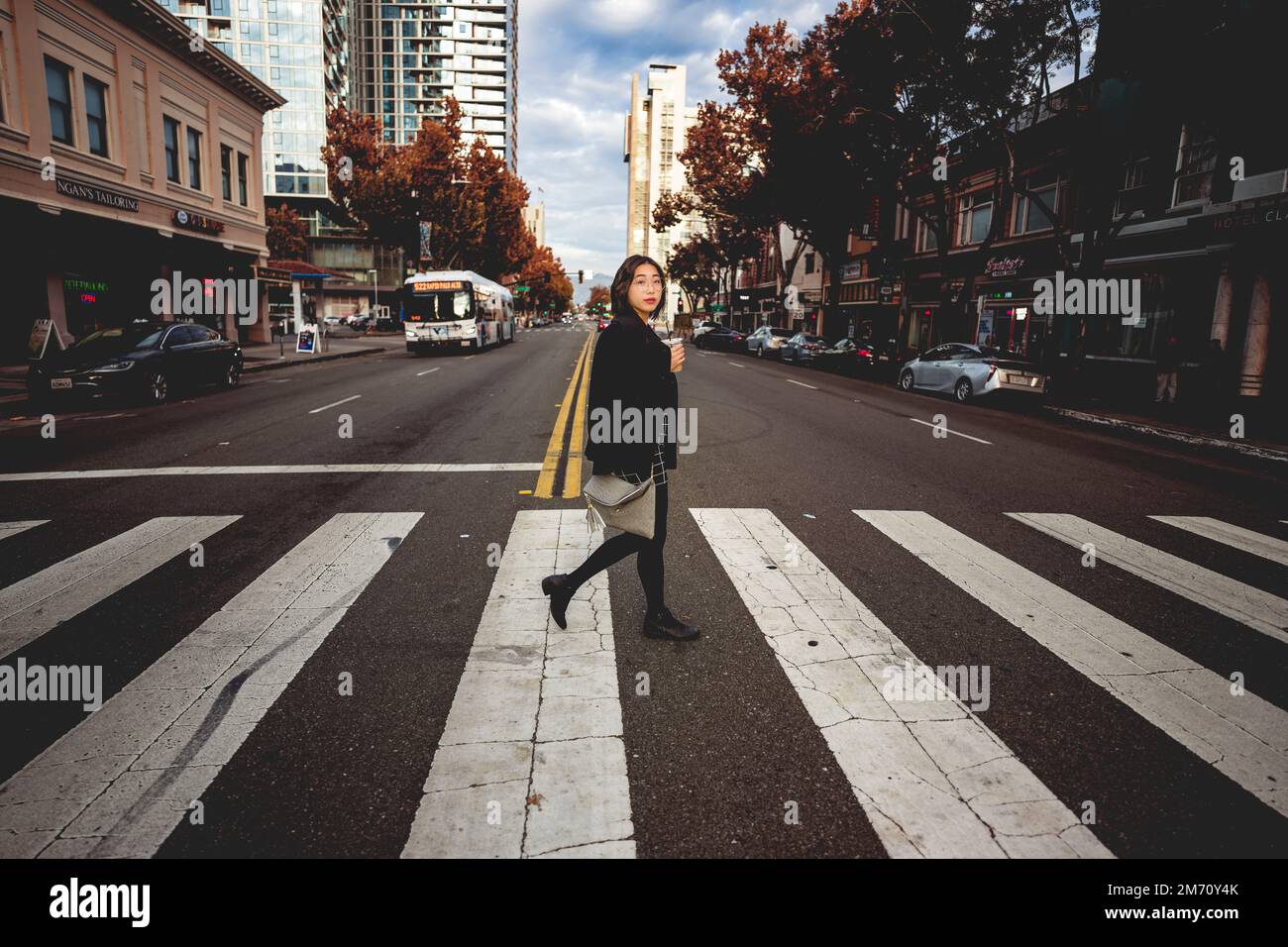 Giovane donna d'affari che tiene la tazza del caffè che attraversa la strada del centro in Zebra Stripe Crossalk Foto Stock