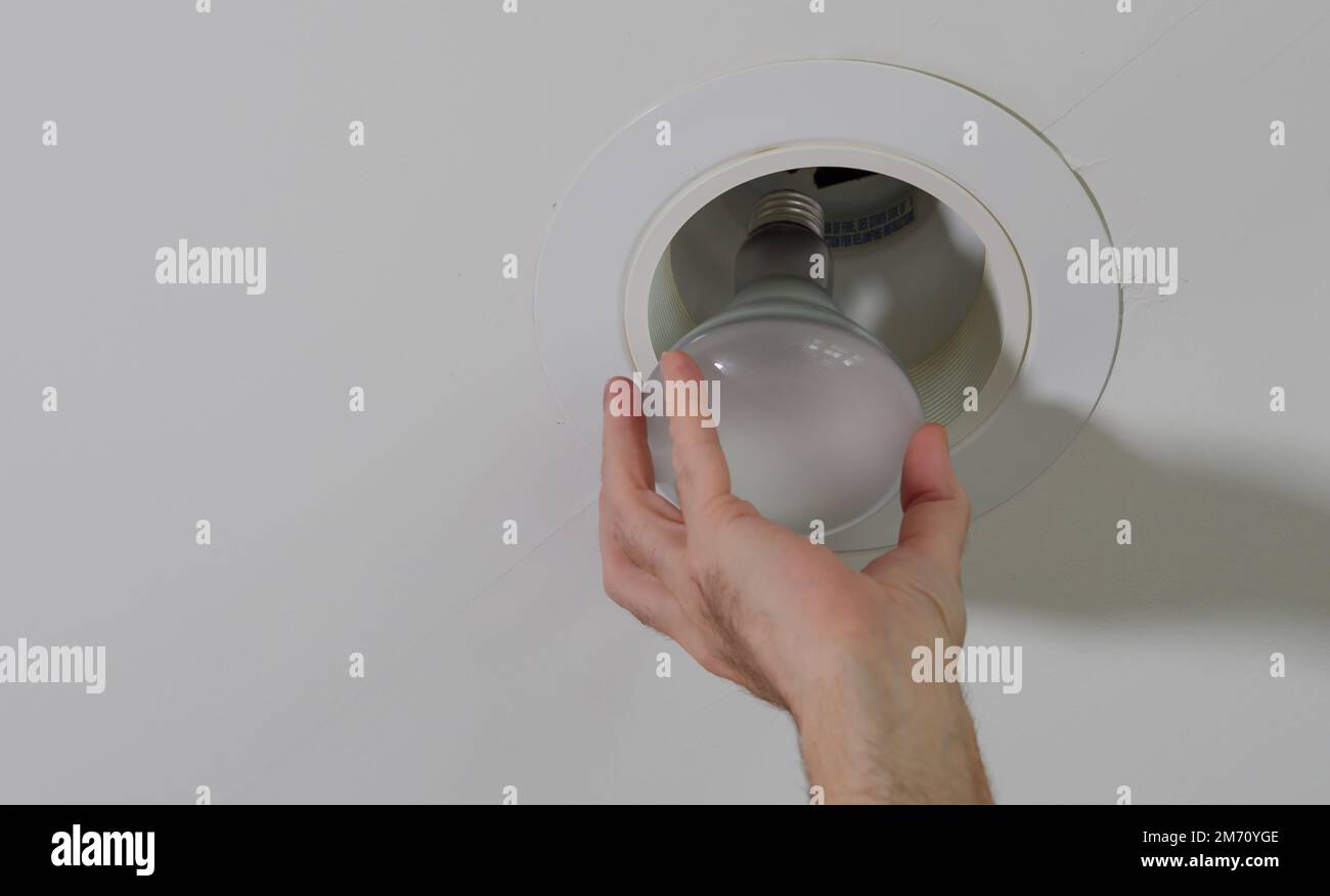 Elettricista che installa una nuova lampadina nel dispositivo di illuminazione da soffitto incassato. Uomo che sostituisce la lampadina a incandescenza bruciata. Foto Stock
