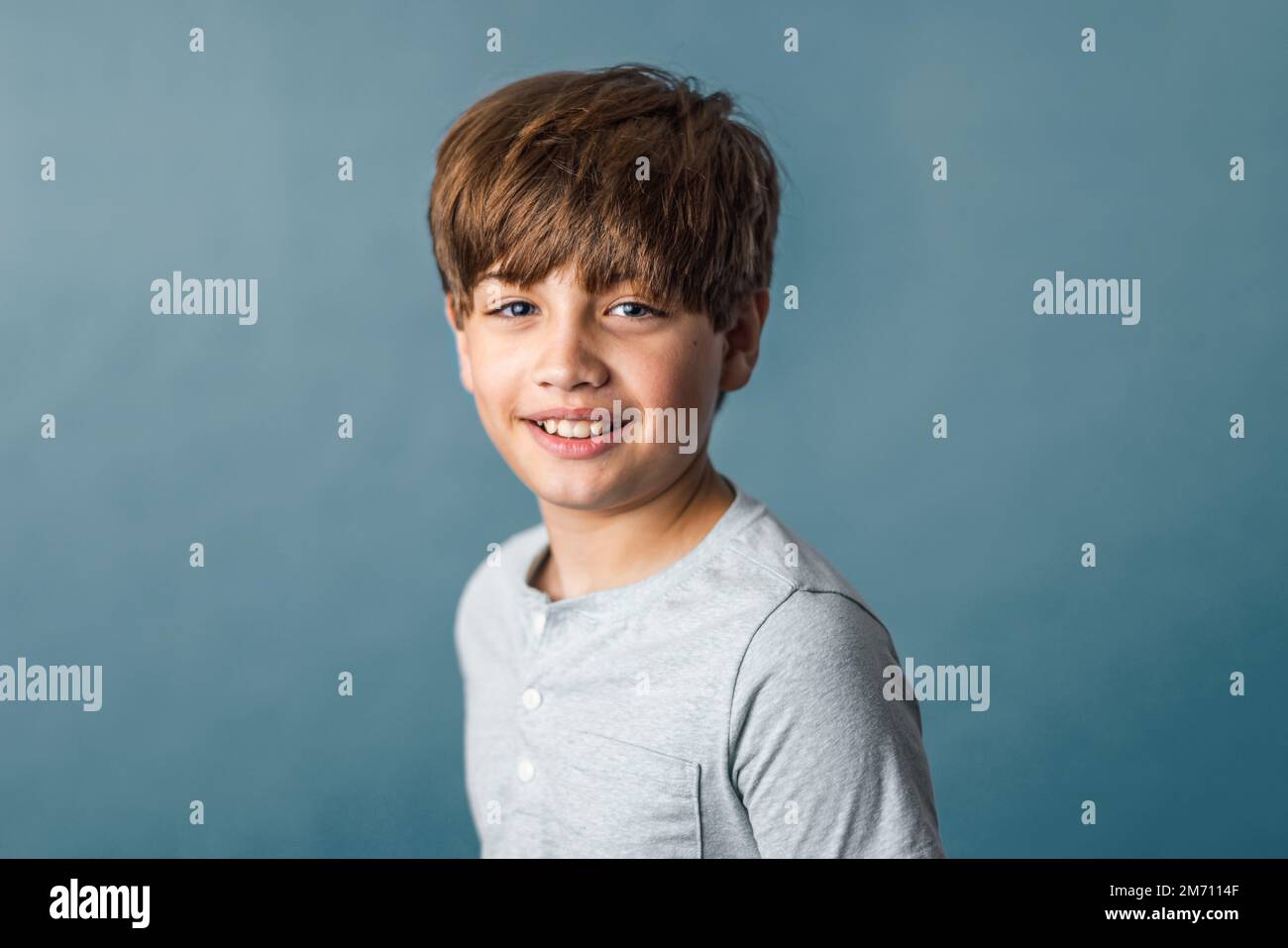 Un grazioso ragazzo pre-teen di Tween dalle spalle in su su su uno sfondo blu muto Foto Stock