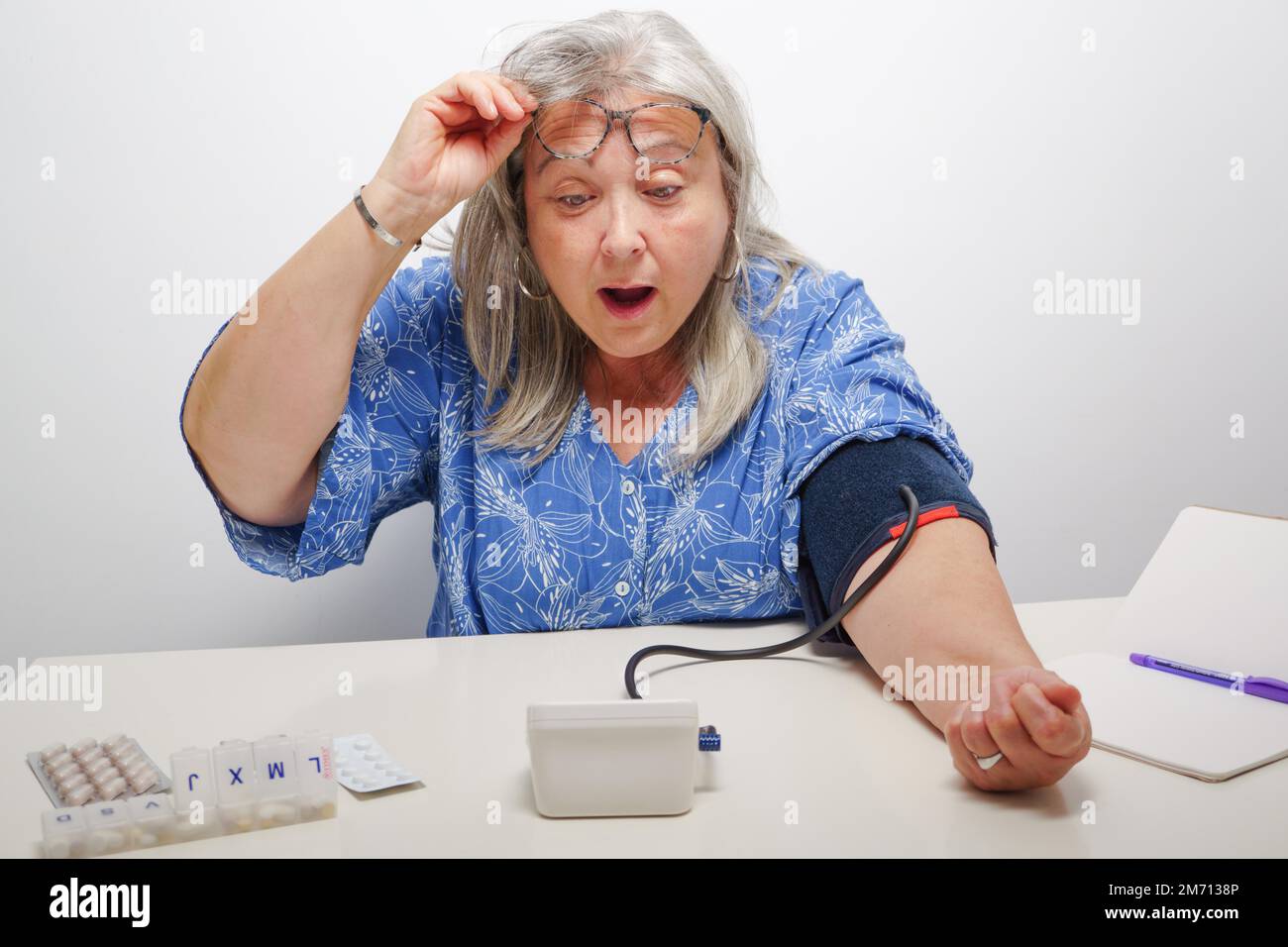 Donna dai capelli bianchi con l'espressione sorpresa quando prende il suo concetto di pressione alta del sangue Foto Stock