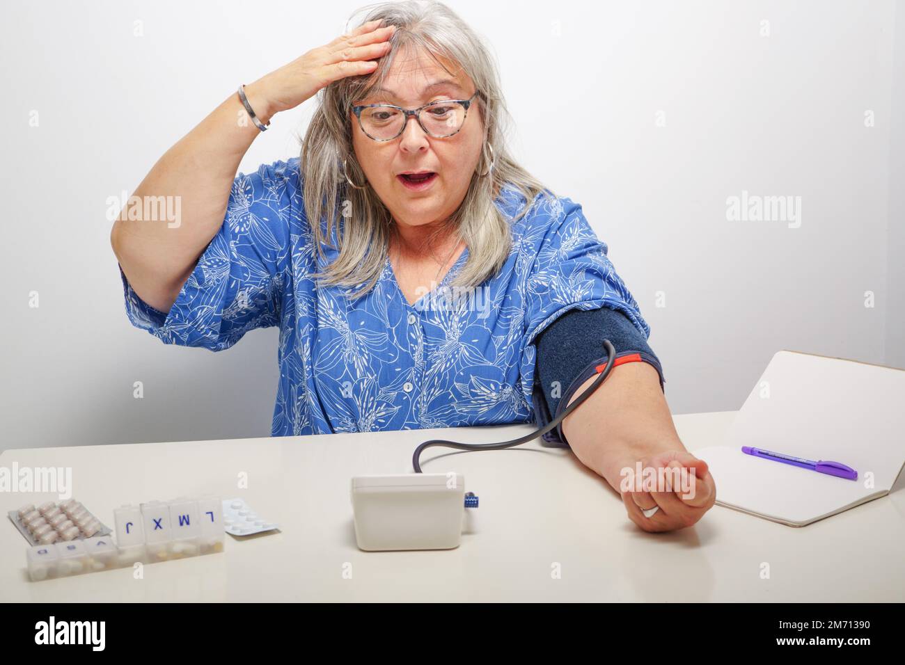 Donna dai capelli bianchi con l'espressione sorpresa quando prende il suo concetto di pressione alta del sangue Foto Stock