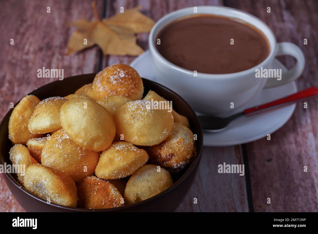 Ciambelle fatte in casa con zucchero in una ciotola e cioccolata calda in una tazza bianca su un tavolo di legno Foto Stock