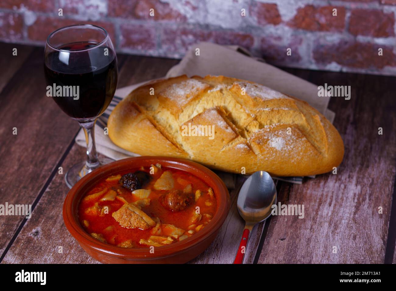 Casseruola di argilla con trippa in umido stile Madrid, piatti tipici spagnoli su un tavolo di legno con un muro di mattoni sullo sfondo Foto Stock