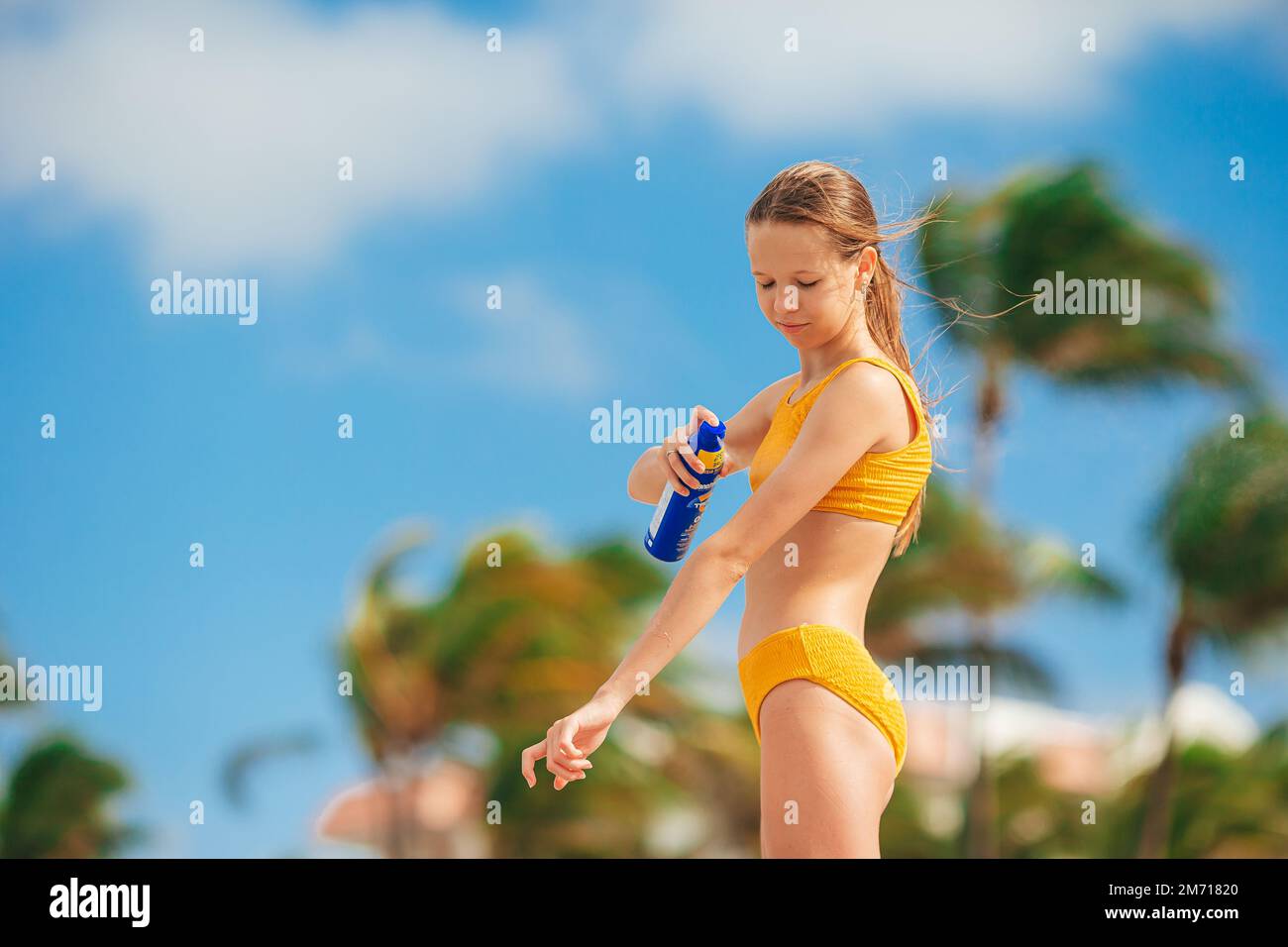 Adorabile ragazza spruzza crema protettiva sul suo corpo in una giornata calda. Protezione solare Foto Stock