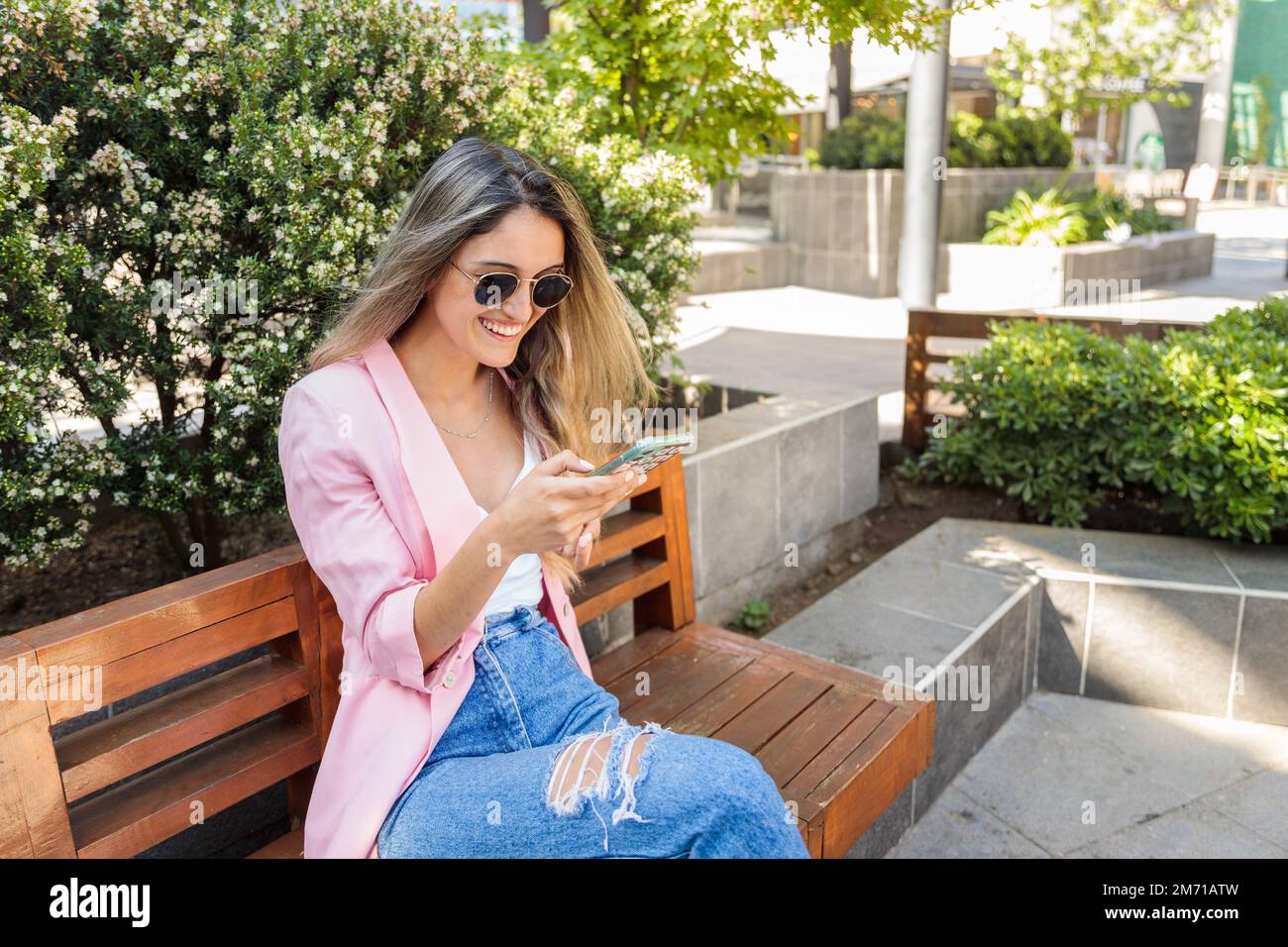 Giovane donna sorridente che usa lo smartphone fuori dal centro commerciale. Dipendenza da Internet e dai social media Foto Stock