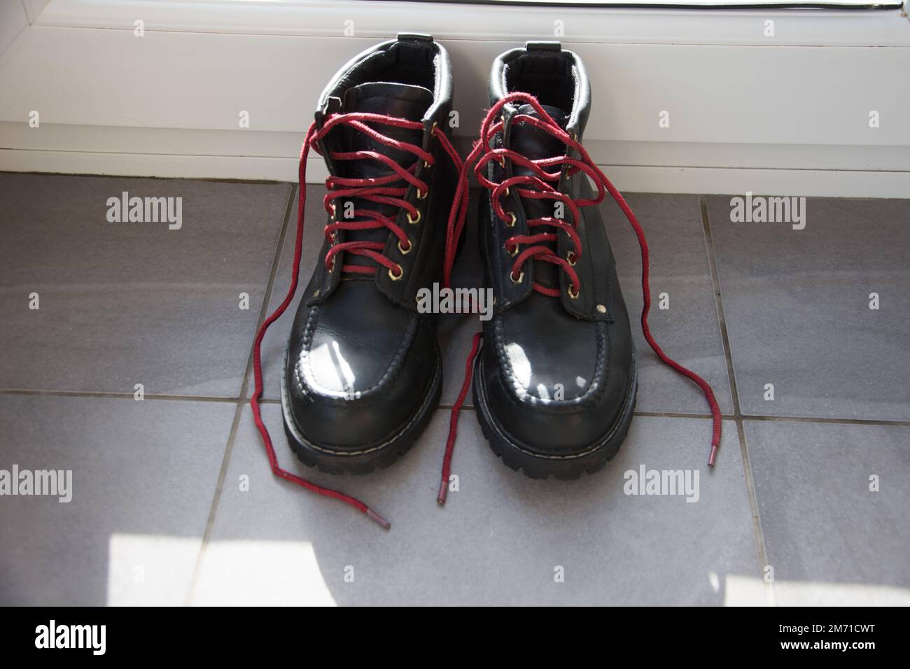 Stivali da passeggio neri con lacci rossi in attesa di pulizia sul pavimento piastrellato grigio con bordo bianco sullo sfondo dopo una giornata di passeggiate nel Lancashire Foto Stock