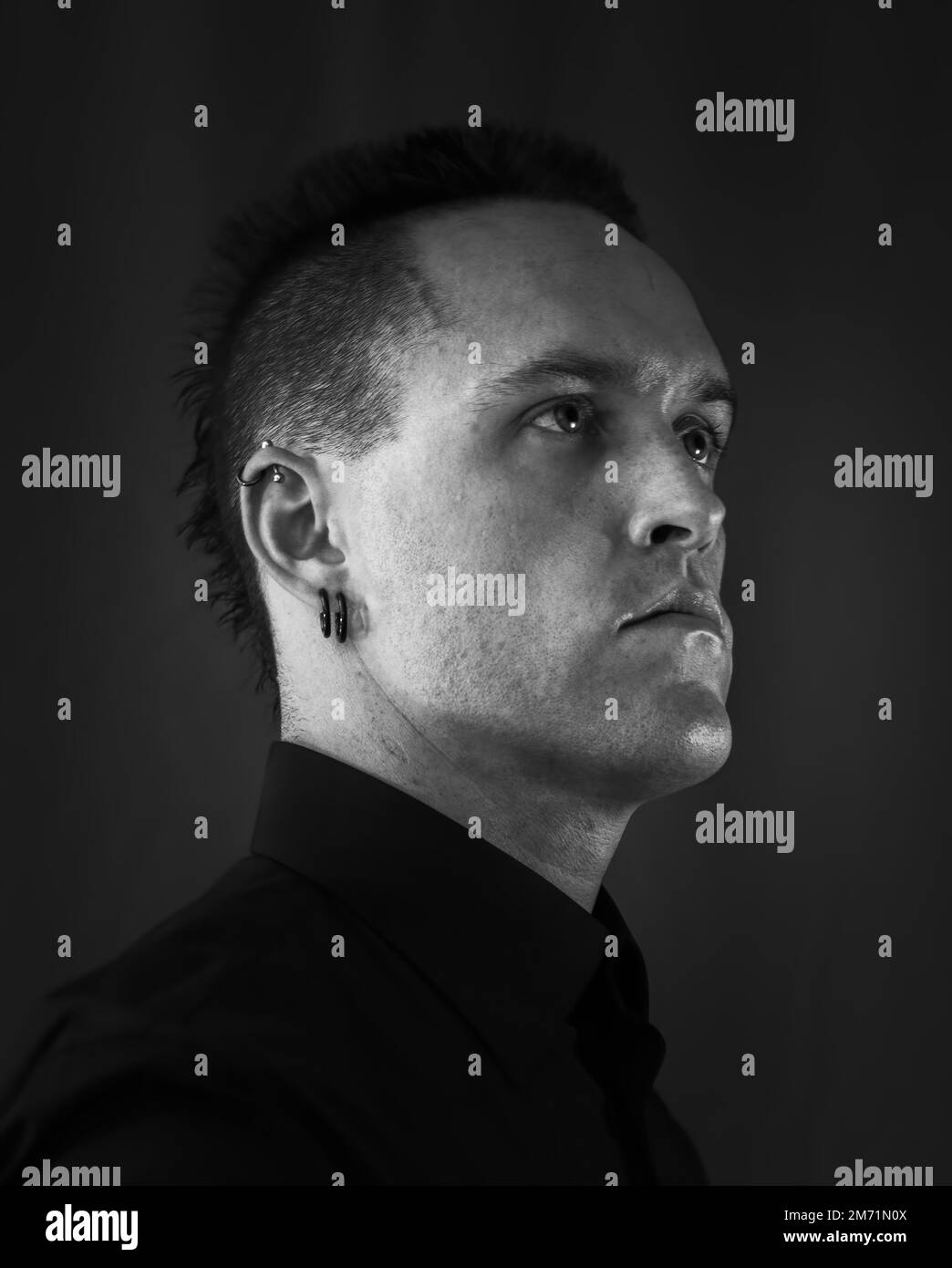Headshot maschile in bianco e nero con un bottone nero su camicia e piercing all'orecchio Foto Stock
