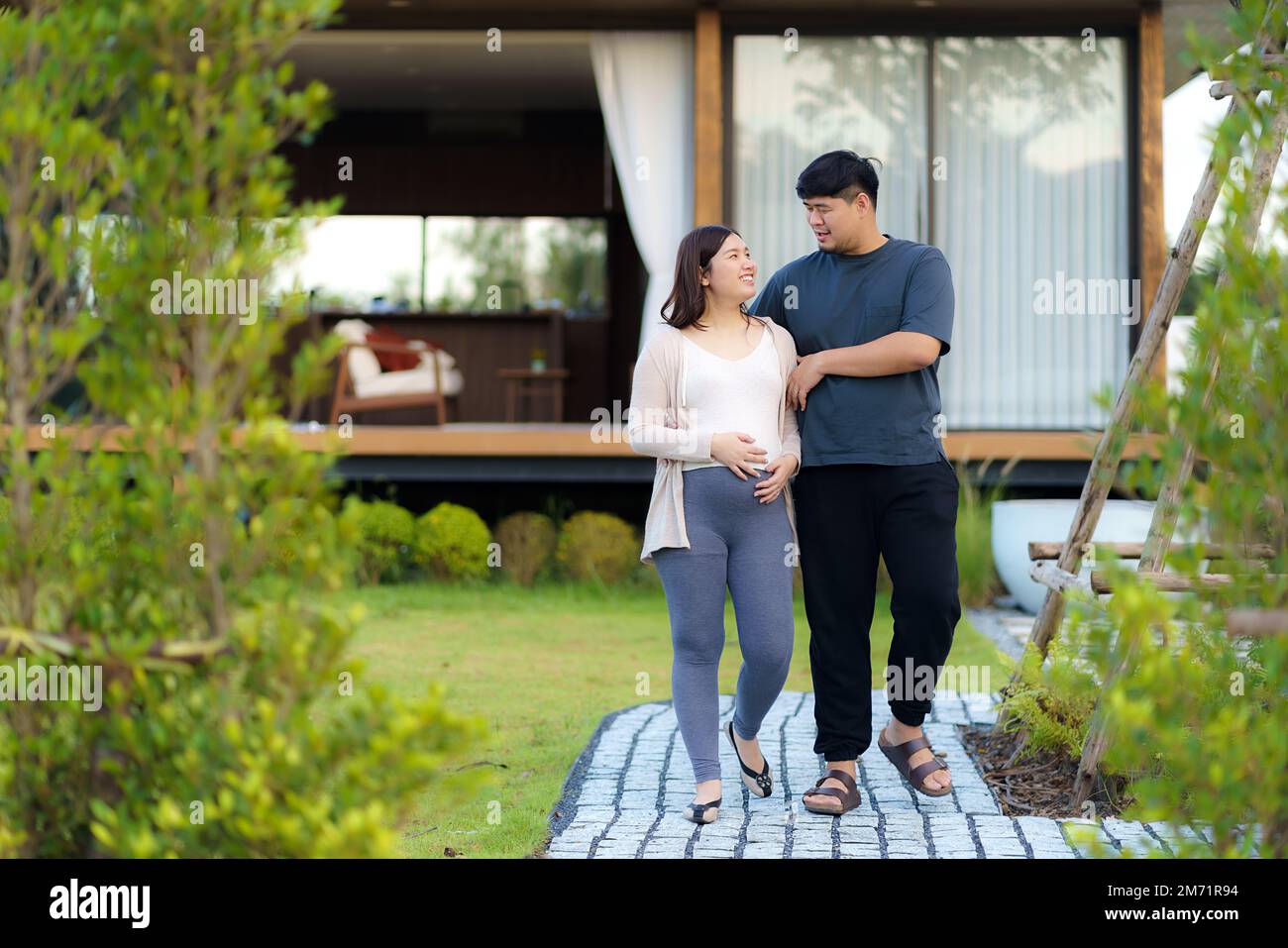Donna asiatica incinta con suo marito che cammina insieme in giardino a casa per rilassarsi e respirare aria fresca. Foto Stock