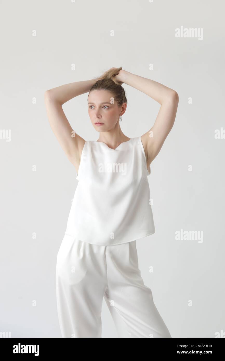 Serie di foto studio di giovane modello femminile in tuta di seta bianca,  blusa senza maniche e pantaloni a gamba larga Foto stock - Alamy