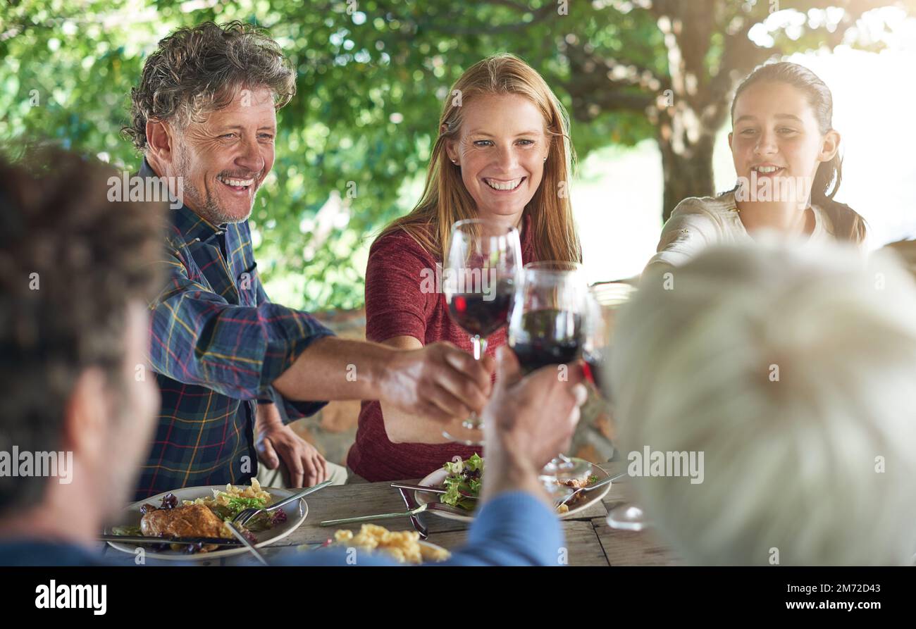 Alla famiglia. un gruppo di persone che preparano la tostatura mentre mangiano il pranzo insieme. Foto Stock