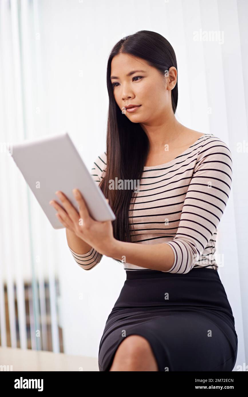 Con l'aiuto del suo tablet, un professionista è in grado di pianificare. Una giovane e attraente donna d'affari asiatica che utilizza un tablet digitale in ufficio. Foto Stock