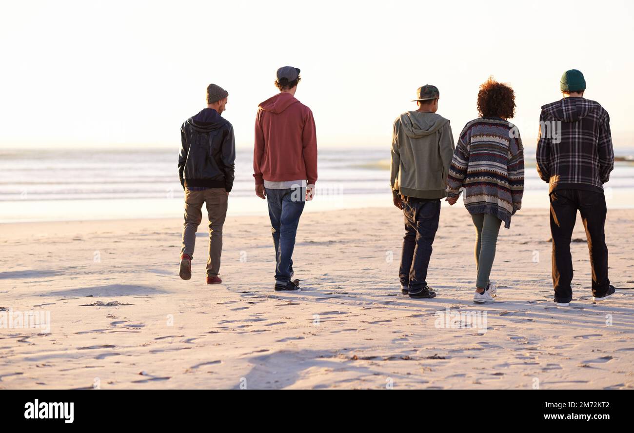 Theres luogo per un altro esploratore. un gruppo di amici che cammina lungo una spiaggia al tramonto. Foto Stock
