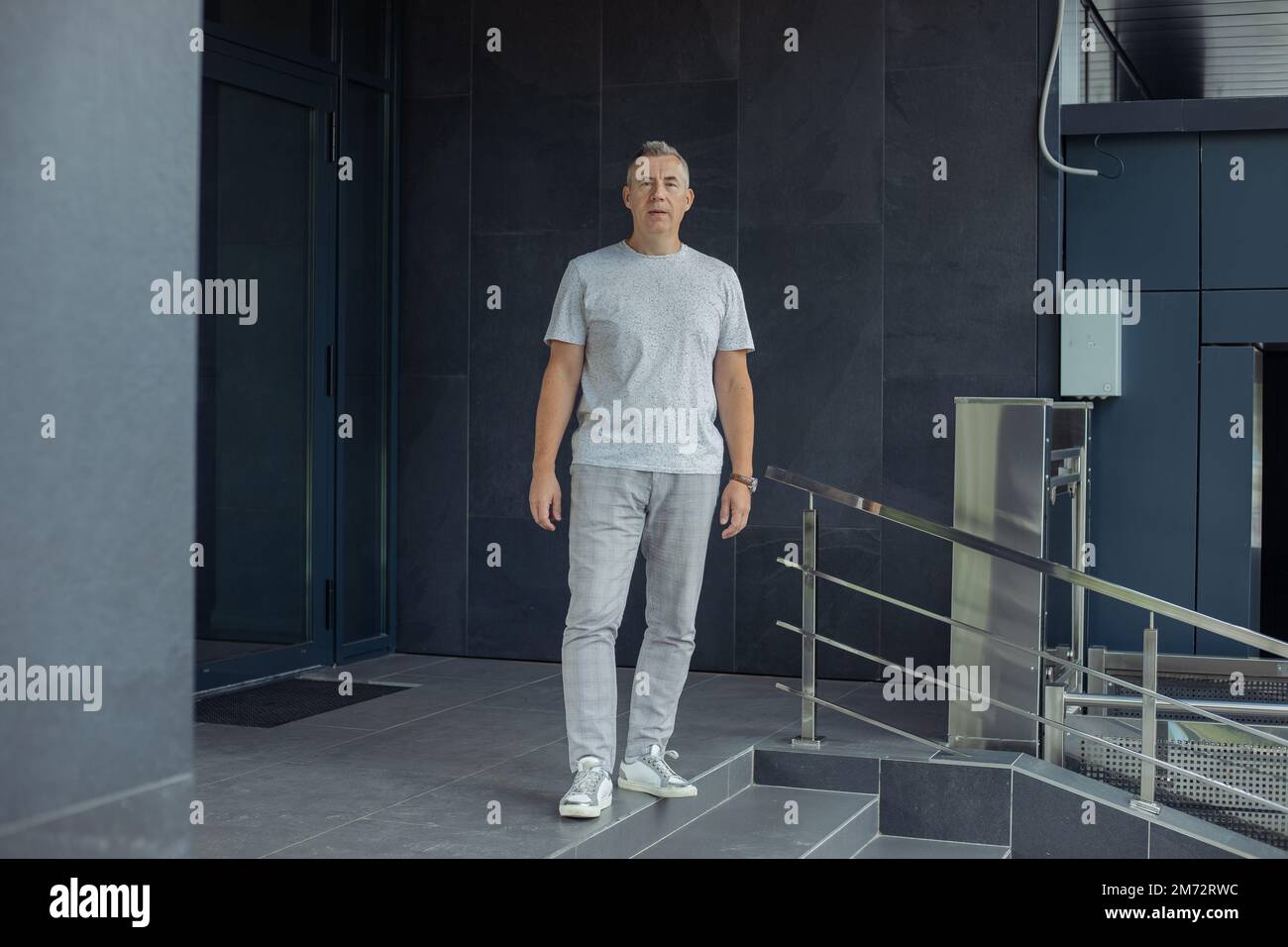 Scatto a tutta lunghezza di uomo fiducioso dai capelli grigi che cammina vicino ai gradini di ingresso dell'edificio. Occupazione del responsabile per gli anziani Foto Stock