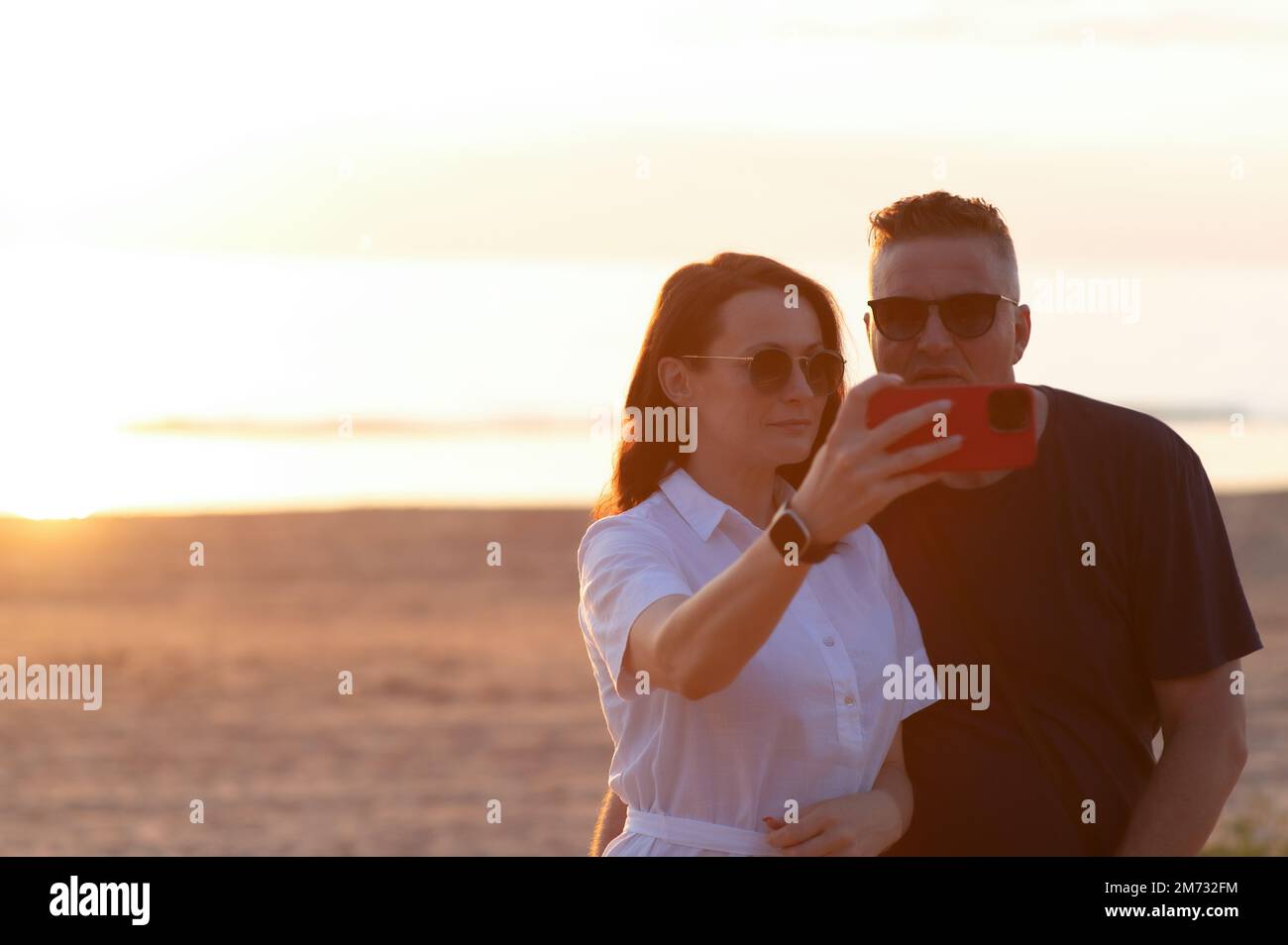 Coppia felice con differenza di età - una giovane donna e un uomo di mezza età prendono un selfie sulla spiaggia Foto Stock