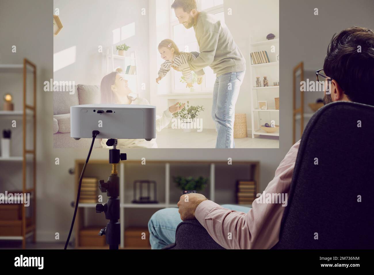 Giovane uomo che guarda un film o le foto di famiglia su un proiettore moderno a casa Foto Stock