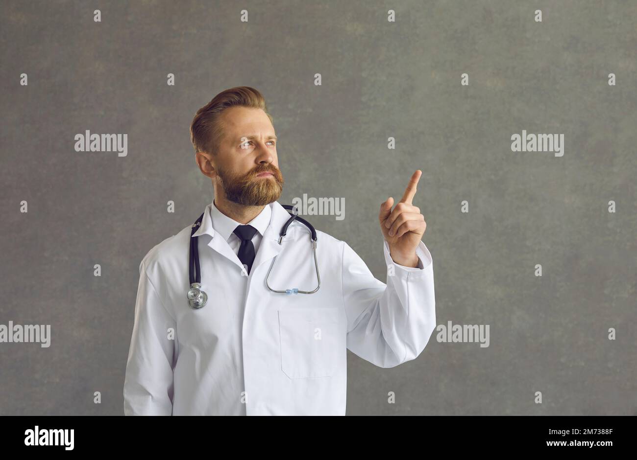 Serio uomo medico mostrando da parte indicando con il dito al grigio spazio copia Foto Stock