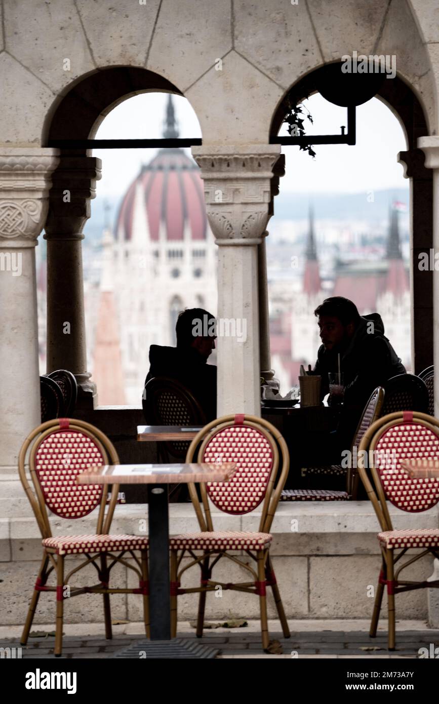 Un'immagine verticale di silhouette di 2 persone sedute in un ristorante con lo sfondo dell'edificio del parlamento di Budapest Foto Stock