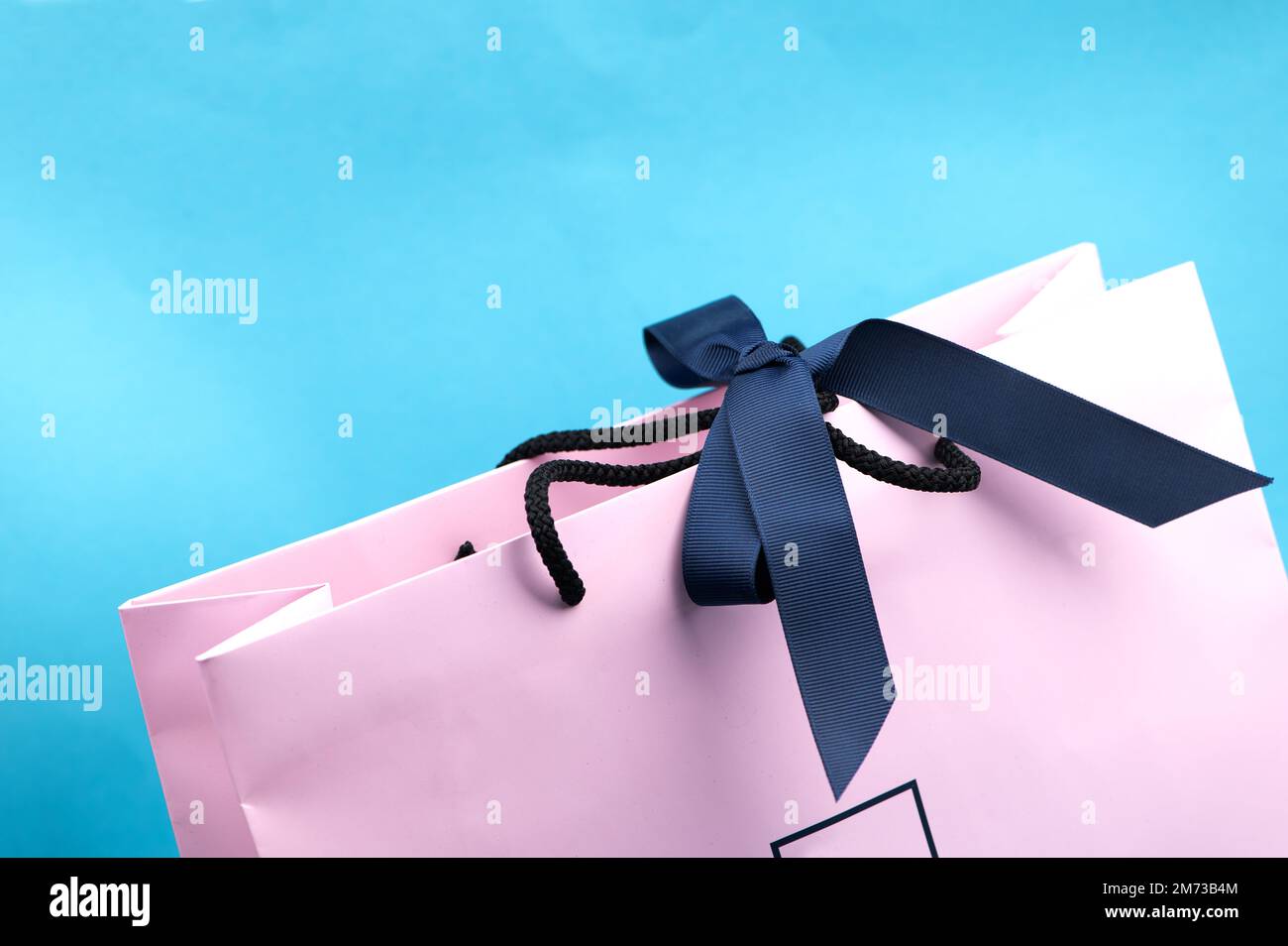 Confezione regalo o shopping color rosa pastello con nastro scuro isolato sul blu Foto Stock