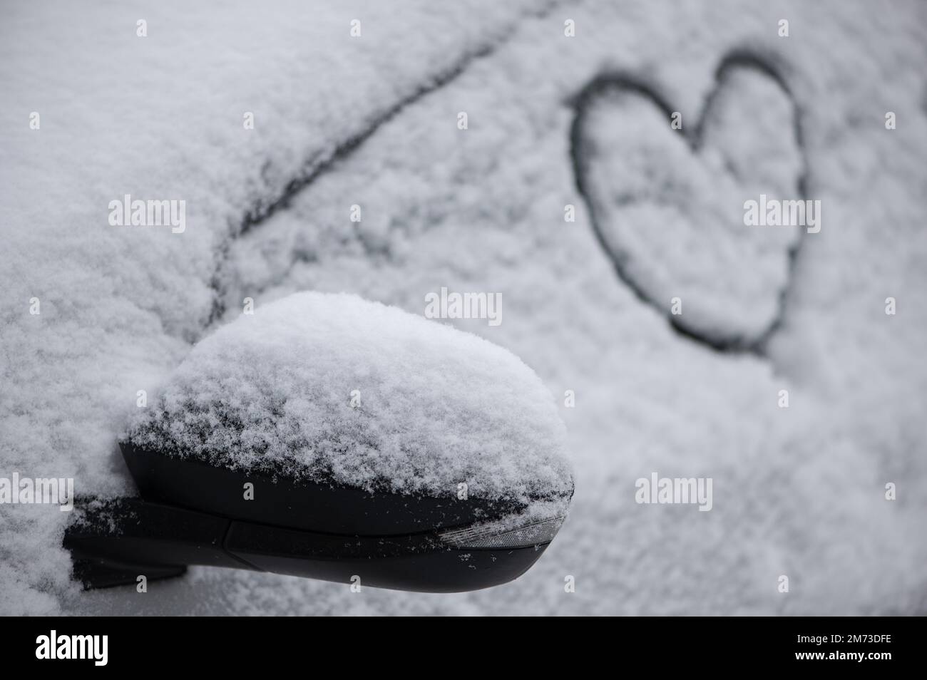 Bel simbolo del cuore disegnato a mano sul finestrino dell'auto innevato alla luce del giorno. Natale e Capodanno concetto Foto Stock